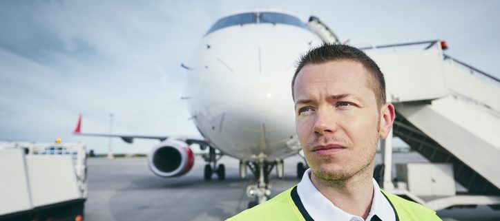 A photo of a ground crew member at the airport in front of a plane
