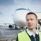 A photo of a ground crew member at the airport in front of a plane