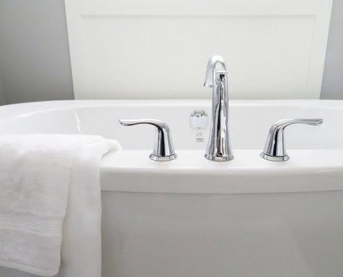 A picture of a bath tub with silver taps and a towel draped over the edge