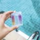 Woman's hand holding a mini water testing kit over blurred swimming pool background